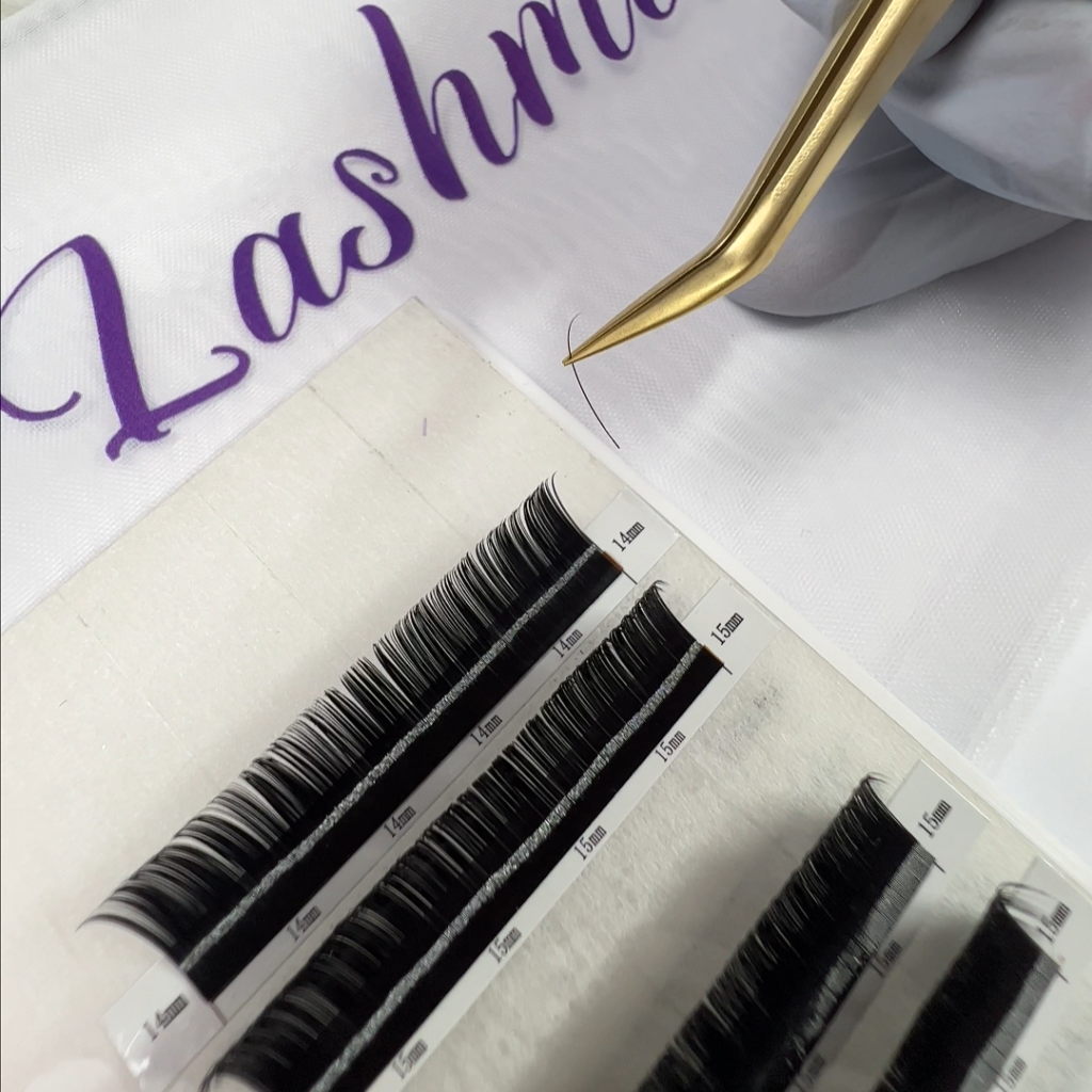 Gold tweezers holding an individual eyelash extension above a tray of Lashmer Classic Lashes labeled with various lengths.