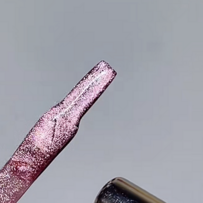 Close-up of a fingernail being painted with shiny pink cat eye gel polish and a magnet held nearby.