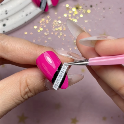 Close-up of applying ACOS nail art stickers on bright pink nails using tweezers.