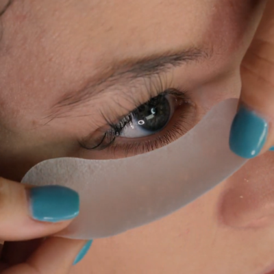 Close-up of a thin gel pad being applied under an eye during an eyelash extension procedure.