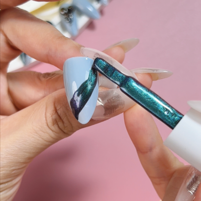 Close-up of applying dark green ACOS Cat Eye Gel polish on a light blue painted nail