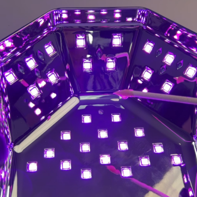 Close-up of the inside of a UV/LED nail lamp with multiple purple LED lights and a nail art tool.