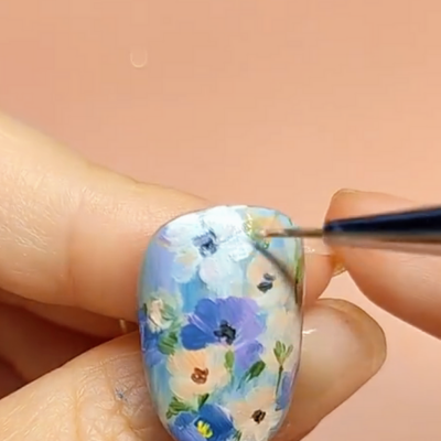 Close-up of a hand holding a finger with detailed floral nail art being painted with a fine brush.