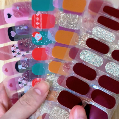 A collection of semi-cured gel nail stickers with various designs held in hand against a wooden background.