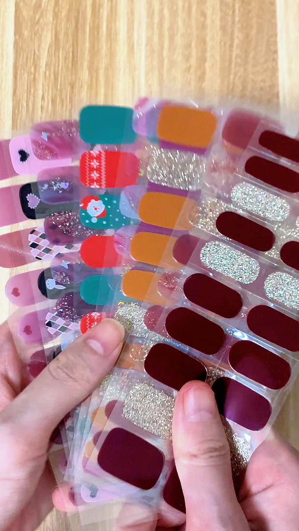 A collection of semi-cured gel nail stickers with various designs held in hand against a wooden background.