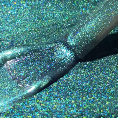 Brush applying glittery green-blue cat eye gel polish with holographic effect