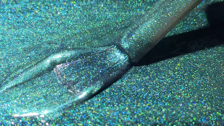 Brush applying glittery green-blue cat eye gel polish with holographic effect