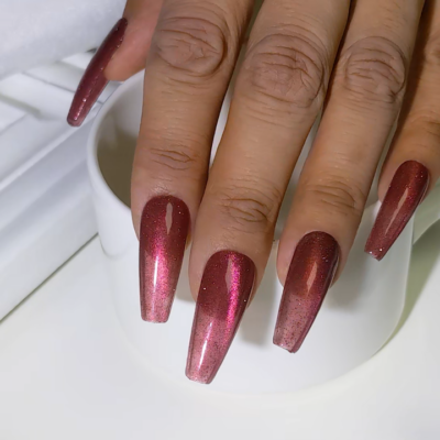 Close-up of long nails painted in shiny, metallic red cat eye gel polish.