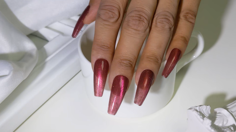 Close-up of long nails painted in shiny, metallic red cat eye gel polish.