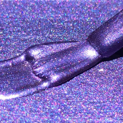 Close-up of a brush applying shiny purple cat eye gel on a glittery surface.