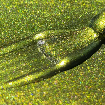 Close-up view of a brush applying glittery green cat eye gel polish with holographic effects.